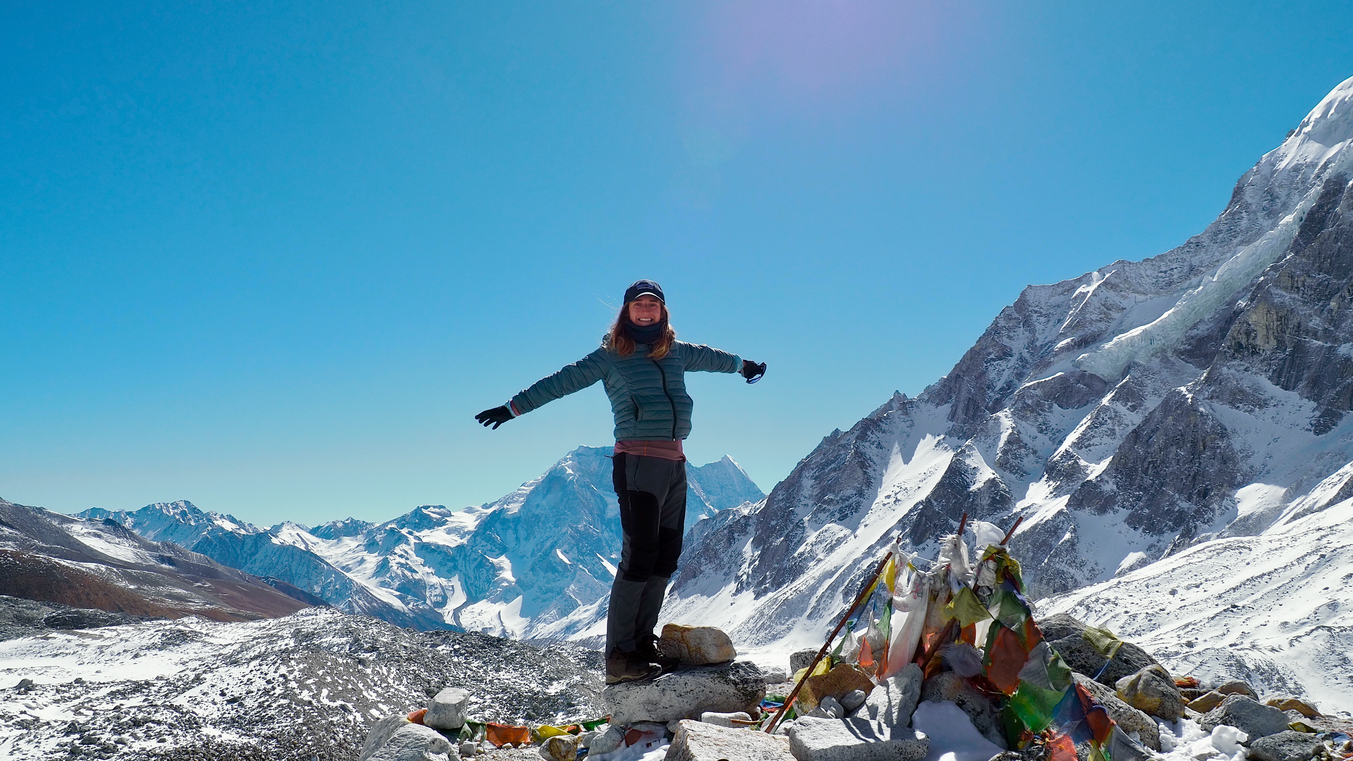 A trekker celebrates beside prayer flags at the summit.